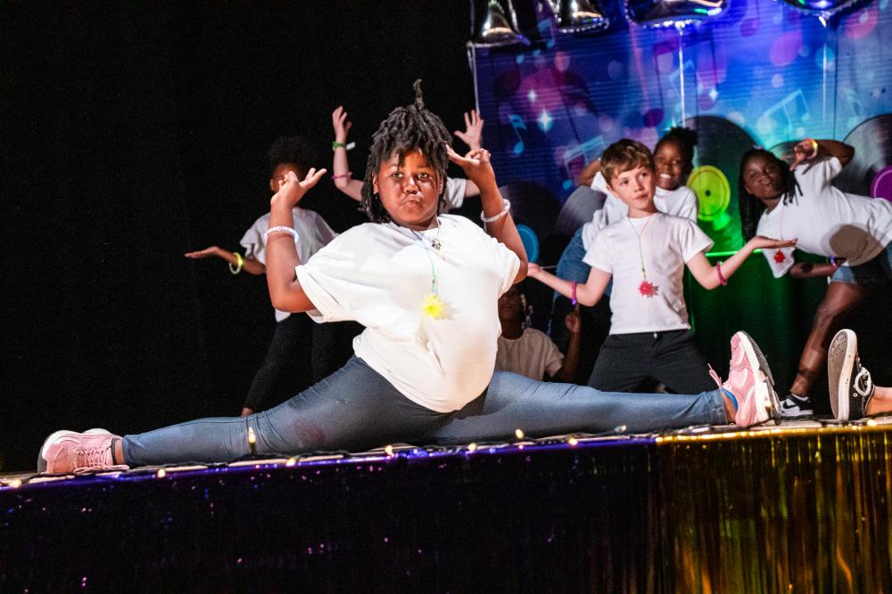 Performer doing a split on stage wearing a white shirt and faux jean leggings