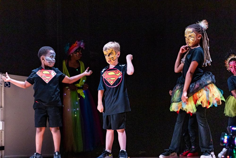 Performers in black costumes with Superman logos on their chests and their faces painted