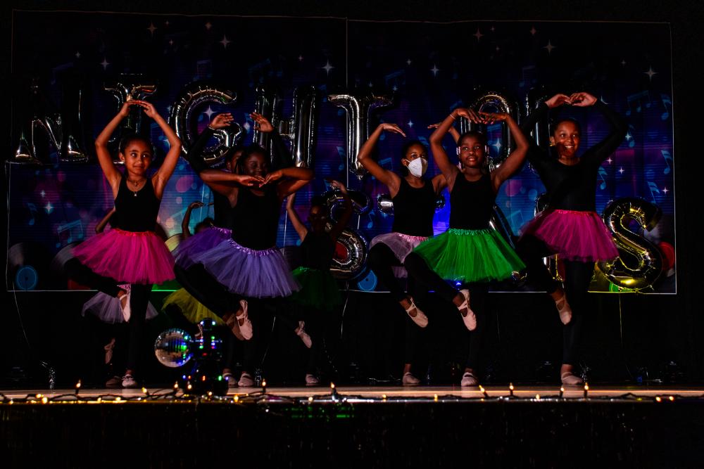 Performers in black with colorful tutus and doing a ballet pose