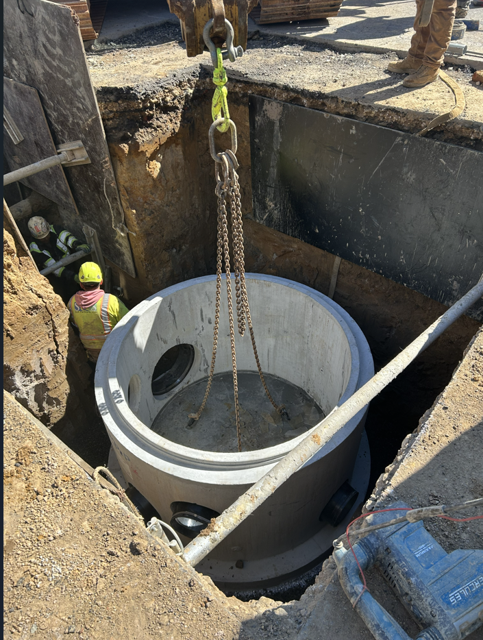 An excavator lowers the new manhole into place on S Pitt Street.