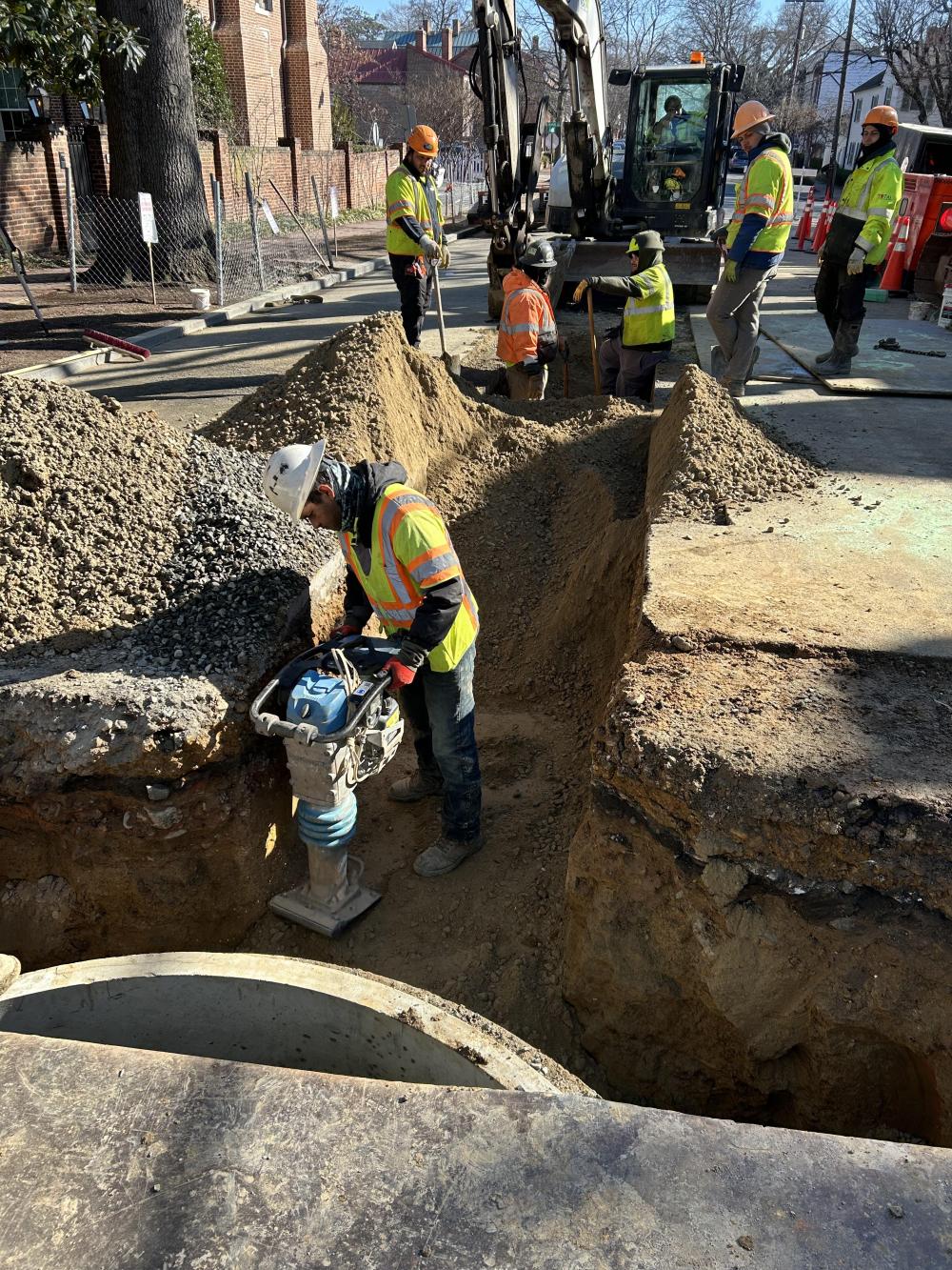 The contractors compact soil near a new manhole.