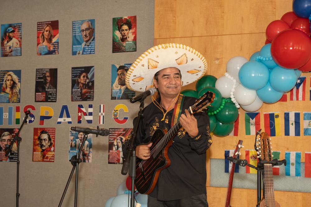 man with sombrero playing guitar with balloons and images of Hispanic icons and hispanic flags in the background