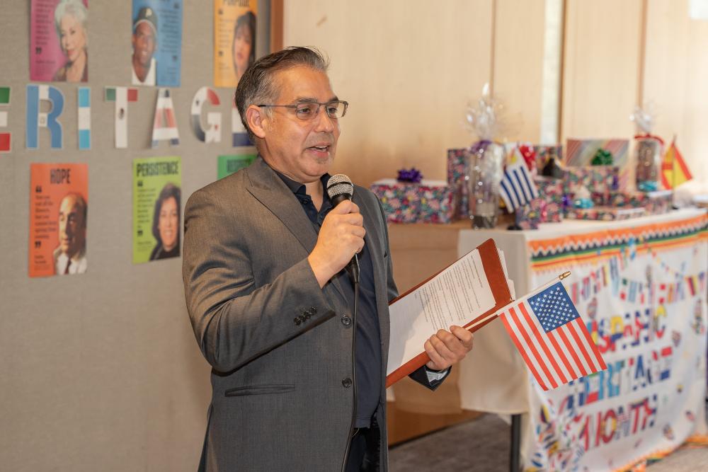 man with microphone talks while holding paper, decorations in background