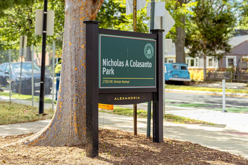 Green Colasanto park sign with black posts situated in front of a tree