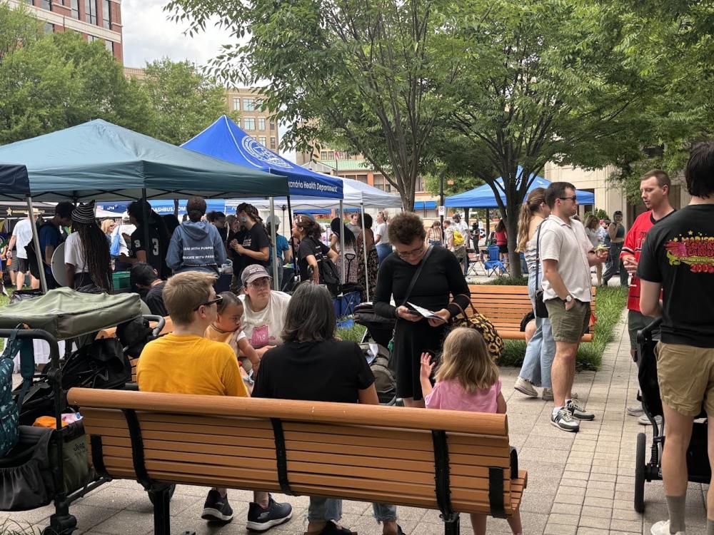 People sitting on bench near row of tents at Alexandria Pride 2026
