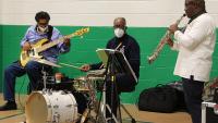 three musicians playing bass guitar, drums and saxophone
