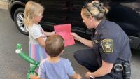 two small children giving a handmade card on red paper to a deputy sheriff