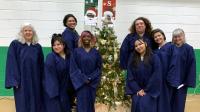 eight women in blue choir gowns standing around a Christmas tree