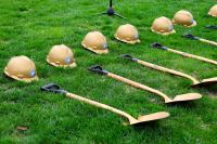 A row of golden hard hats and shovels lying on the grass in anticipation of the tree planting ceremony