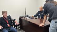 Civilan sitting in chair with polygraph equipment attached, deputy at desk looking at screen and another civilian leaning over desk and watching