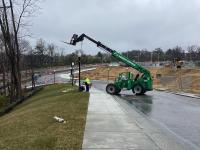 Photo of light pole being lowered into place next to a sidewalk along Road 7 on March 27, 2024