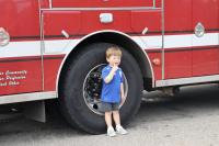 Little child wearing a blue shirt standing by the fire truck's back wheel