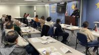 Sheriff's Office commander in blue uniform standing a podium and speaking to several community members in a classroom setting