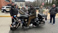 Deputy in blue uniform allowing community member to sit on his agency motorcycle while other community members look on