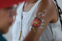  A close-up of a person’s upper arm featuring a colorful face painting of a hibiscus flower. 
