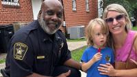 Sheriff's commander in blue uniform with resident and small child at National Night Out, all smiling