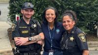Two deputies in blue uniforms standing next to Mayor who is in the center, all smiling