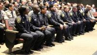 Rows of recruit deputies, some in blue uniforms and some in tan, seated at their graduation ceremony
