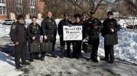 several deputies in blue winter uniforms holding sign that says Meals on Wheels with lots of snow in the background