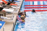 Kids in the deep end of the pool by the diving platforms engaged in a swim class