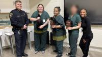 Sheriff and braiding instructor standing with three students in the middle who are holding mannequin heads with braided hair