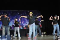 Kids dressed in black and jeans dancing on stage and an adult female also dancing on stage