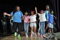 Kids wearing casual clothes and holding hands with staff on stage