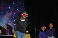 Young girl dressed in a black shirt and jeans with big, pink rimmed glasses