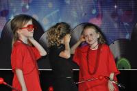 Three girls on stage with 2 girls wearing red clothing and one girl in the middle wearing black