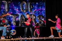 Performer in the middle holding a red, blow up guitar, while other performers are kneeling down around him