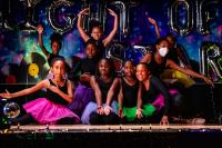 Performers in black sitting on the stage with colorful tutus and posing