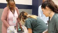 Two inmates in green uniforms looking at information while a member of Friends of Guest House assists them at the Reentry Resource Fair