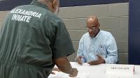 Inmate in green uniform that says Alexandria Inmate on the back speaking with a member of Arm & Arm peer support group at Reentry Resource Fair