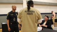 Deputy in a blue uniform, inmate wearing a tan uniform that says Alexandria inmate on the back, and a business representative interacting with each other at a reentry resource fair
