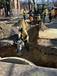 The contractors compact soil near a new manhole.