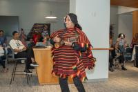 man playing guitar wearing black flowered hat and striped red and yellow poncho with people watching in the background