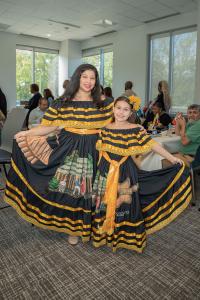 mother and daughter with black and yellow dresses standing and smiling at the camera showing off skirt artwork with onlookers in the background