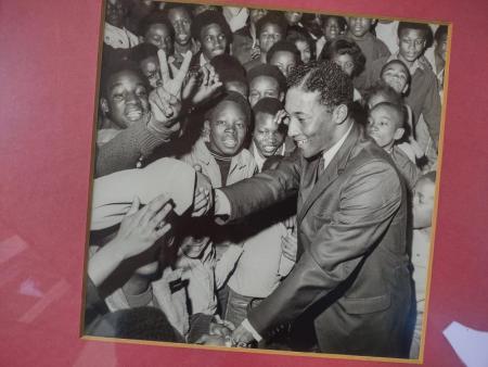 Black and white photo on maroon background, Ira Robinson shaking hands in a crowd.