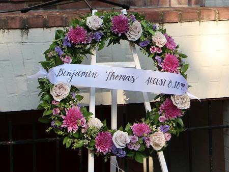 a memorial wreath with pink, white and purple flowers and a banner reading: Benjamin Thomas August 8, 1899