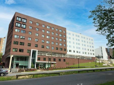A seven-story apartment building partially build into a hill. The half of the building closer to the viewer is red brick, while the other half of the building is white stone.