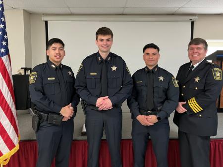 Three deputies in blue uniforms standing next to Sheriff in formal blue uniform with U.S. flag to left and Virginia flag to right