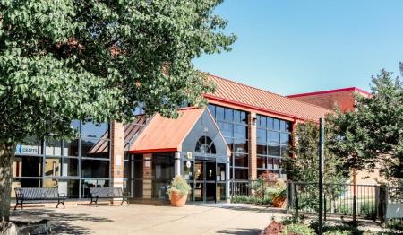Front of the Chick Armstrong recreation center on a sunny day, framed by trees and plants.