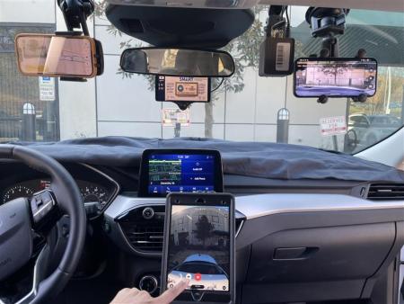 The interior of a vehicle. Mounted to the windshield and on the console are small screens and camera equipment.