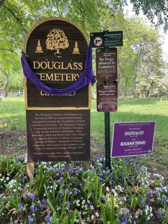 The Douglass Cemetery sign is draped with a purple cloth. At the base, a temporary purple sign commemorates Joseph McCoy and Benjamin Thomas who were lynched in Alexandria in the 19th&nbsp;century.