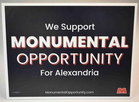 A printed white on black poster reads, “We Support Monumental Opportunity For Alexandria.”
