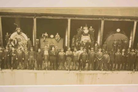 A portion of a panoramic black-and-white photograph from 1940 shows R.F. & P. railroad employees posing in front of engines at Potomac Yard. Some pose on the equipment, while most men form a line in front.