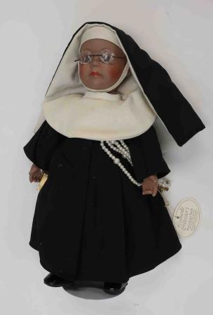 A porcelain doll depicts an Black nun, wearing a black and white nun’s habit and glasses.