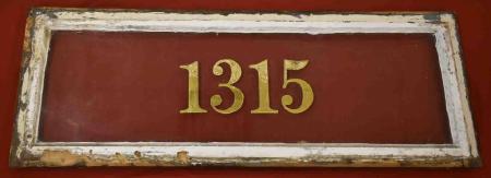 This dark red wooden panel has gold lettering with the street number 1315 and a raised white border.