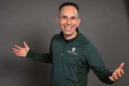 man smiling with green jacket arms outstretched