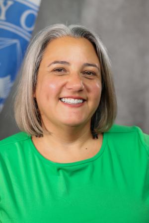A woman with shoulder length hair and a green shirt smiles brightly.